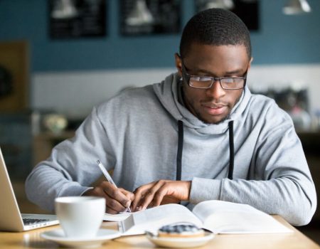 A young Black man studying in glasses and a hoodie.
