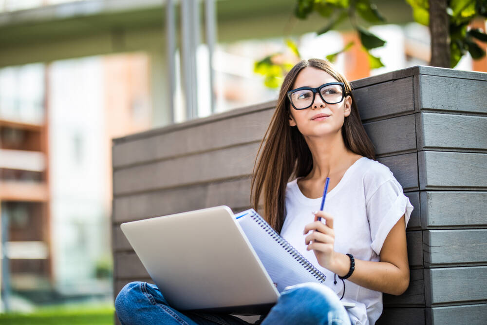 A girl with long hair and glasses studying outside.